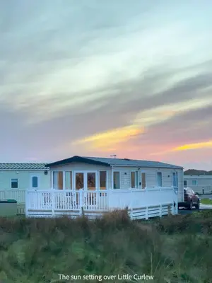 a white house with a sun setting over a little church at Little Curlew, Ynyslas, Borth in Borth