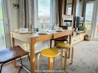 a dining table with chairs and a television in a room at Little Curlew, Ynyslas, Borth in Borth