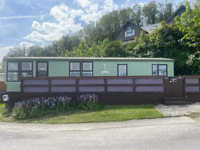 a small house behind a fence with purple flowers at Haven on the Hill 2 Bed Caravan with Town Views of Aberystwyth F7 in Aberystwyth