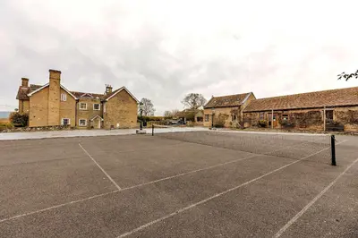 an empty tennis court in front of a building at Finest Retreats - The Walton in Onibury