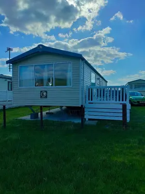 a tiny house sitting in the grass with a porch at M&C Caravan Hire Sunnysands in Barmouth