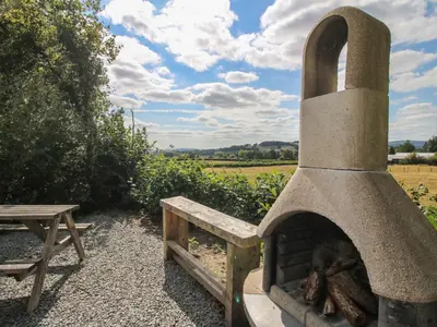 a stone oven next to a table and a field at Aston - Shepherd Hut in Craven Arms