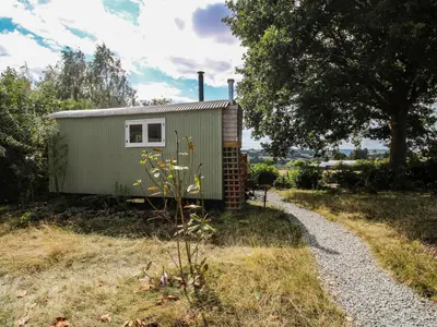 a green tiny house sitting on top of a field at Aston - Shepherd Hut in Craven Arms