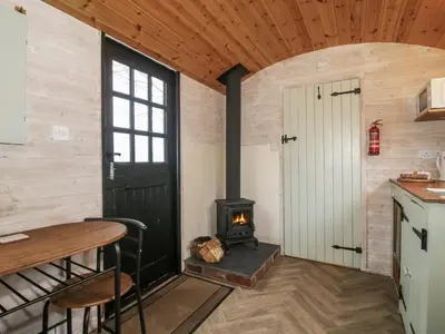 a room with a stove and a table and a door at Aston - Shepherd Hut in Craven Arms