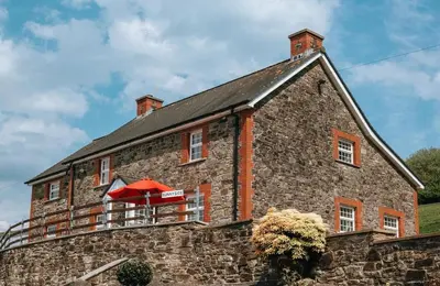 a large brick building with a red umbrella on it at Luxury 5-Bed Farmhouse - Sleeps 8 & Hot Tub in Brecon