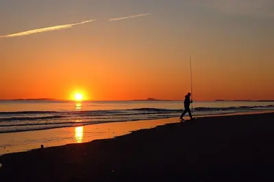 a man walking on the beach at sunset at Beach Front Apartment in Tywyn in Tywyn