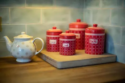 four red containers on a wooden shelf with a tea pot at Garden House in North Lydbury