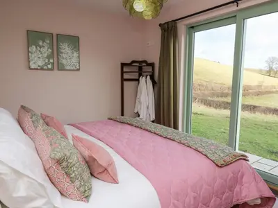 a bedroom with a bed with pink sheets and a window at Dol Blodau in Llandrindod Wells