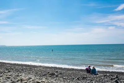 two people sitting on the beach looking at the ocean at Tan Y Bryn in Llanrhystyd