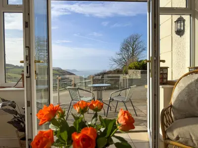 an open door to a patio with orange flowers at Crogal Farmhouse in New Quay