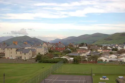 a tennis court with houses and mountains in the background at Trem Y Mor - Edge of the Sea in Tywyn