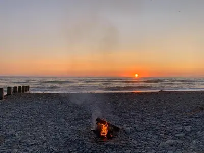 a bonfire on the beach with the sunset in the background at Trem Y Mor - Edge of the Sea in Tywyn