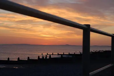 a view of the ocean from a fence at sunset at Trem Y Mor - Edge of the Sea in Tywyn