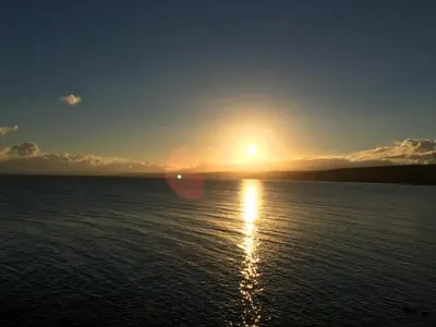 a sun setting over the water with a ship at Min y Graig New Quay in New Quay