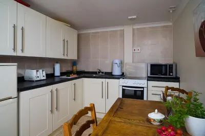 a kitchen with white cabinets and a wooden table at Min y Graig New Quay in New Quay
