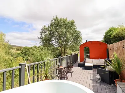 a deck with a red shed and a table and chairs at Red Kite at Wild Valley Huts in Oswestry