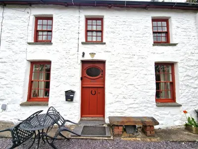 a red door on a white building with a bench at Arwel Llangrannog in Llanllwchaiarn