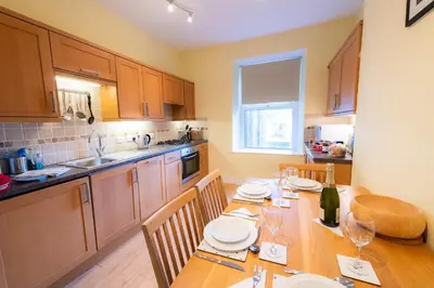 a kitchen with a wooden table with plates and wine glasses at Plas Hafan Apartment 2 Aberystwyth in Aberystwyth