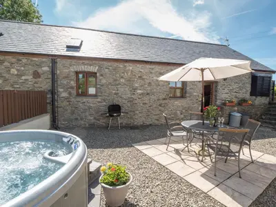 a patio with a hot tub and a table and chairs at Eirlys Aberystwyth in Llanrhystyd