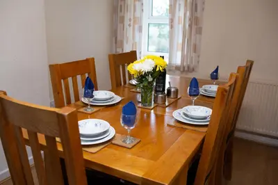 a wooden table with chairs and plates and a vase of flowers at Soar Cottage Aberystwyth in Aberystwyth