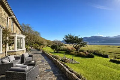 a house with a patio with chairs and a lawn at Glandwr hall - 6 Bed - Magnificent Country House with Heated Swimming Pool & Jacuzzi in Barmouth