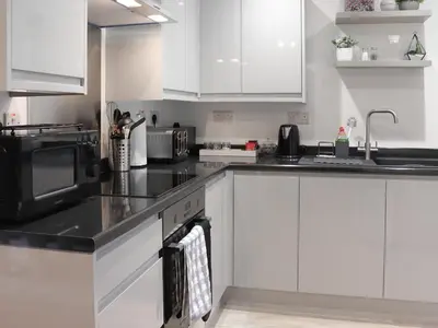 a kitchen with white cabinets and black counter tops at Llety Cariad in Bala