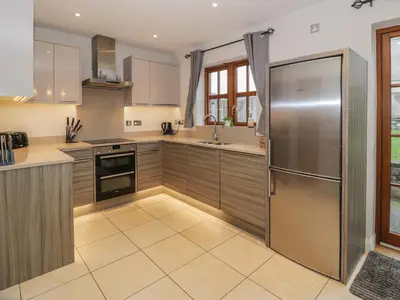 a kitchen with wooden cabinets and a stainless steel refrigerator at Anadlu in Llanbedr