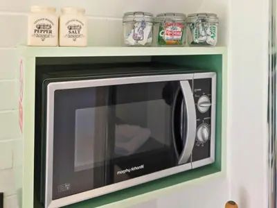 a microwave on a wall with a shelf above it at The Kingfishers Burrow in Llandovery