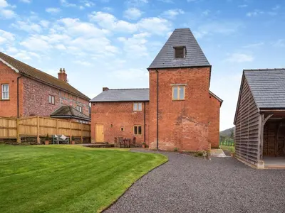 an old brick building with a grey roof and a yard at Nupton Hop Kiln in Kings Pyon