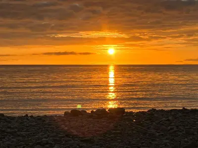a sunset on the beach with the sun setting at Cosy caravan Sunbeach in Llwyngwril