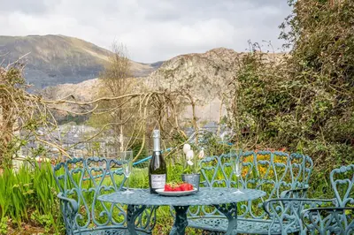 a table with a bottle of wine and some chairs at Pen-Y-Bryn Cottage in Blaenau-Ffestiniog