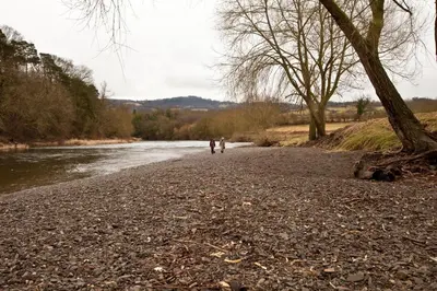 two people walking along a river with trees at Hay Retreats in Hay-on-Wye