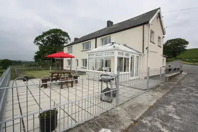 a fence in front of a house with a picnic table at Cob Cottage in Tregaron