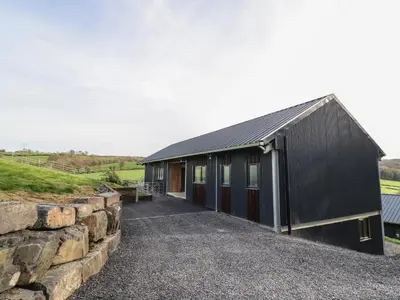 a black building with a stone wall next to it at Bwncath in Welshpool