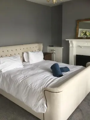 a white bed with white pillows and a fireplace at Harbour House in Barmouth