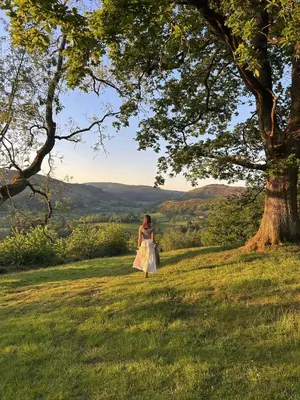 a woman in a dress standing in a field next to a tree at Cyra in Llangollen