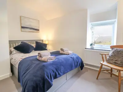 a bedroom with a bed with blue sheets and a window at Ty Dyffryn in Blaenau-Ffestiniog