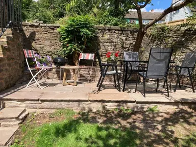 a patio with chairs and a table and a stone wall at Ty Bach Coch in Scethrog
