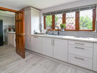 a kitchen with white cabinets and a sink and windows at Pondarosa in Llandrindod Wells