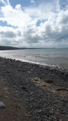 a beach with rocks and the ocean on a cloudy day at Brynarfor near Aberaeron in Llanon
