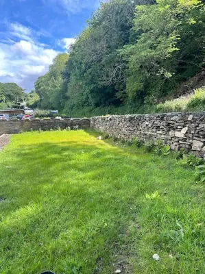 a stone wall next to a field of green grass at Kimberly House in Arthog