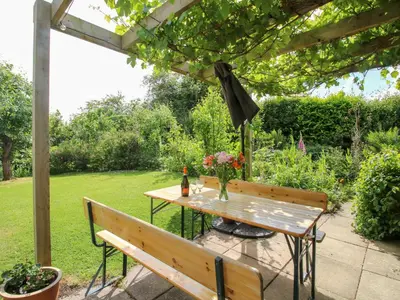 a table and bench under a pergola in a garden at Plum Hill in Oswestry