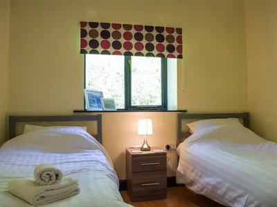 two beds in a bedroom with a window and a lamp at Heyope Cottage in Llangunllo