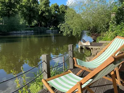 two lawn chairs sitting next to a river with a boat at Riverbank in Shrewsbury