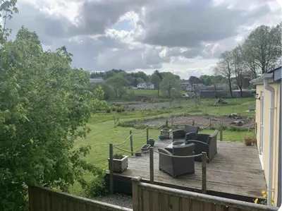 a wooden deck with couches and chairs on a field at Drws Y Coed in Tal-gareg