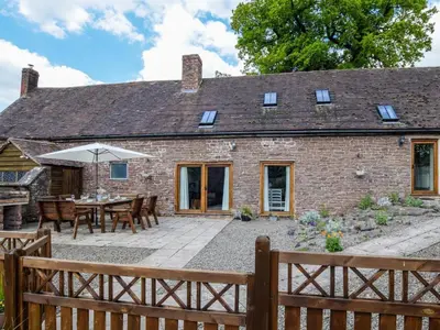 an external view of a brick cottage with a table and umbrella at 5 Bed in Craven Arms oc-95212 in Tugford
