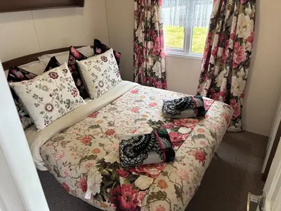 a small bedroom with a bed with a floral bedspread at Stunning Pet Friendly 2 bed StaticCaravan in Clarach Bay 2017 model in Aberystwyth