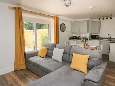 a living room with a gray couch and a kitchen at Garden View in Llanybydder