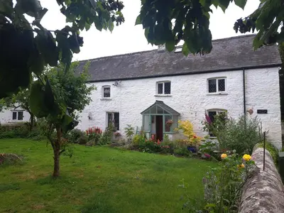 a white cottage with a garden in front of it at Ty Gwyn Farmhouse in Brecon
