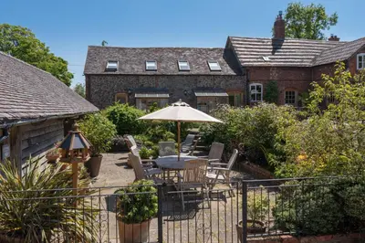 a patio with a table and umbrella in front of a house at Daisys Place at Middle Farm and Cottages in Picklescott